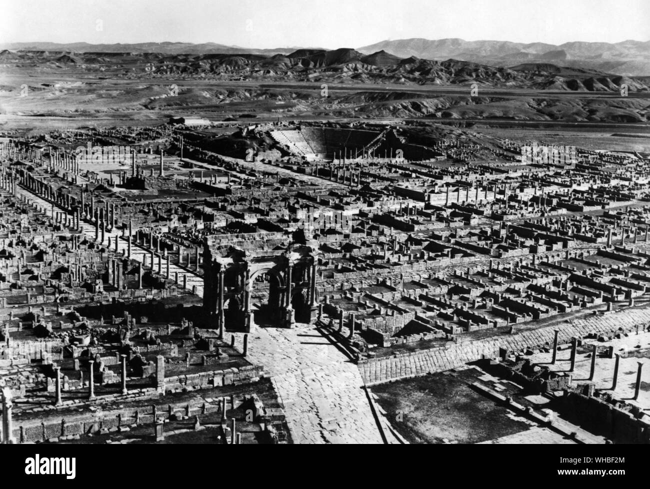Timgad - Vista dal west end della città che mostra l'Arco di Traiano, forum e il teatro, con la Aures montagne sullo sfondo - Timgad era un romano città coloniale in Africa del Nord fondata dall'Imperatore Traiano intorno al 100 D.C. Le rovine sono degni di nota per essere uno dei migliori esempi pervenutici della pianta a griglia come usato nella città romana pianificazione.. Foto Stock