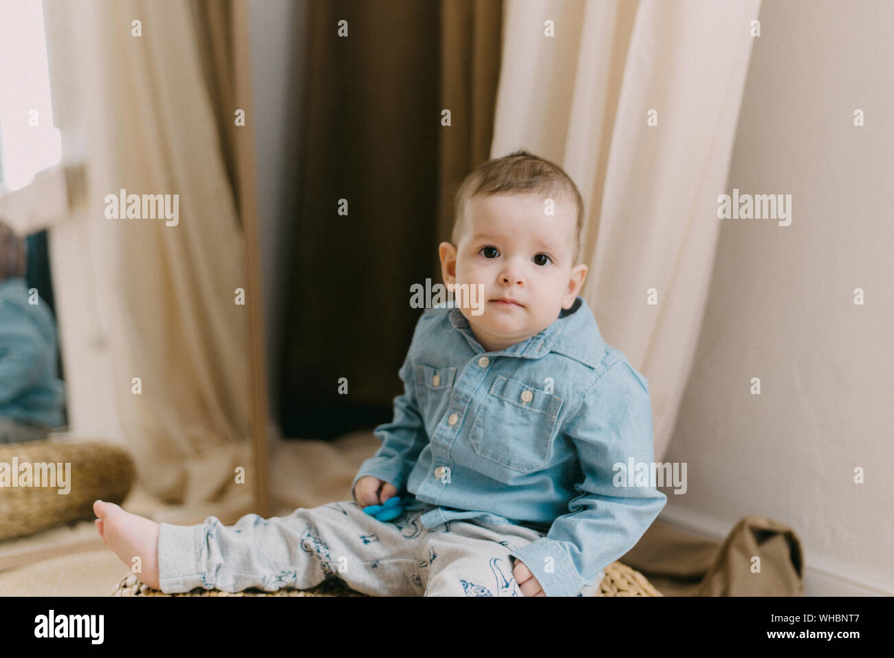 Bambino di un anno in una camicia denim siede su un puff beige. Un bambino in un dolce impostazione. il fuoco selettivo Foto Stock