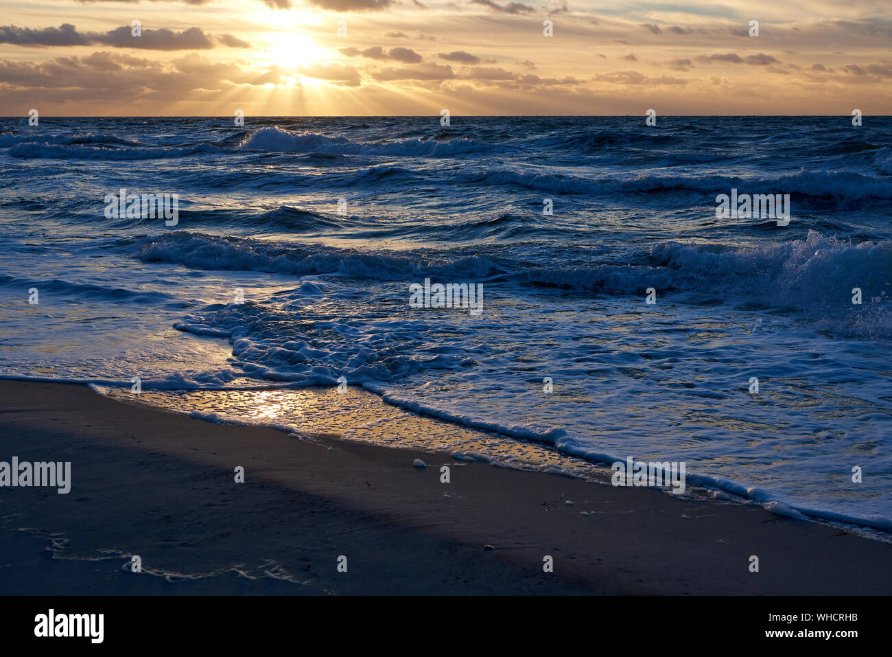 Pittoresco e colorato tramonto sul Mar Baltico, con nuvole e riflessi luminosi sulle piccole onde sulla spiaggia di sabbia. Foto Stock