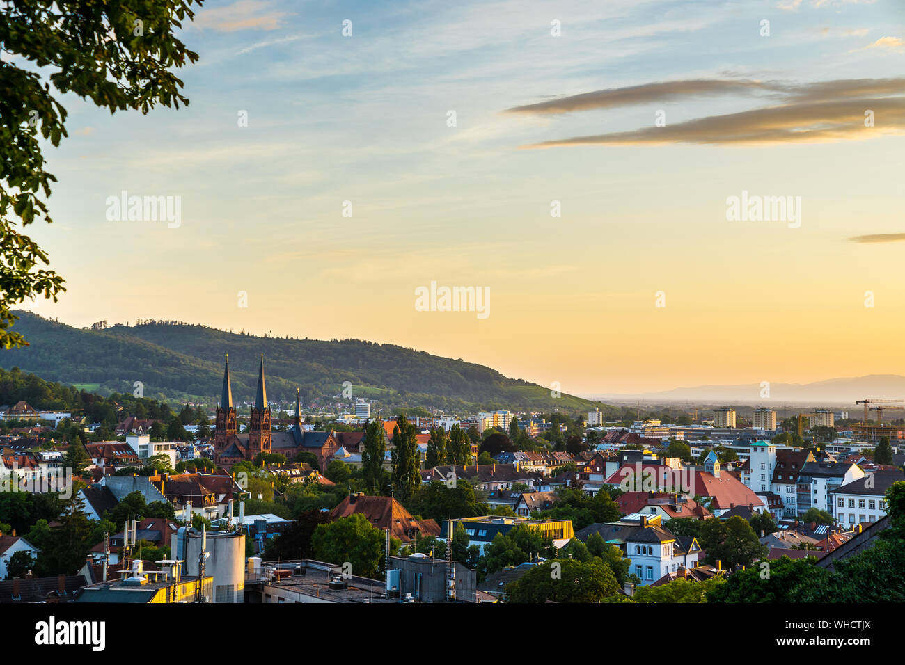 Germania, caldo arancio luce del tramonto sulla skyline della città al di sopra di Freiburg im Breisgau nella foresta nera natura paesaggio che circonda la bella johanneskirche c Foto Stock