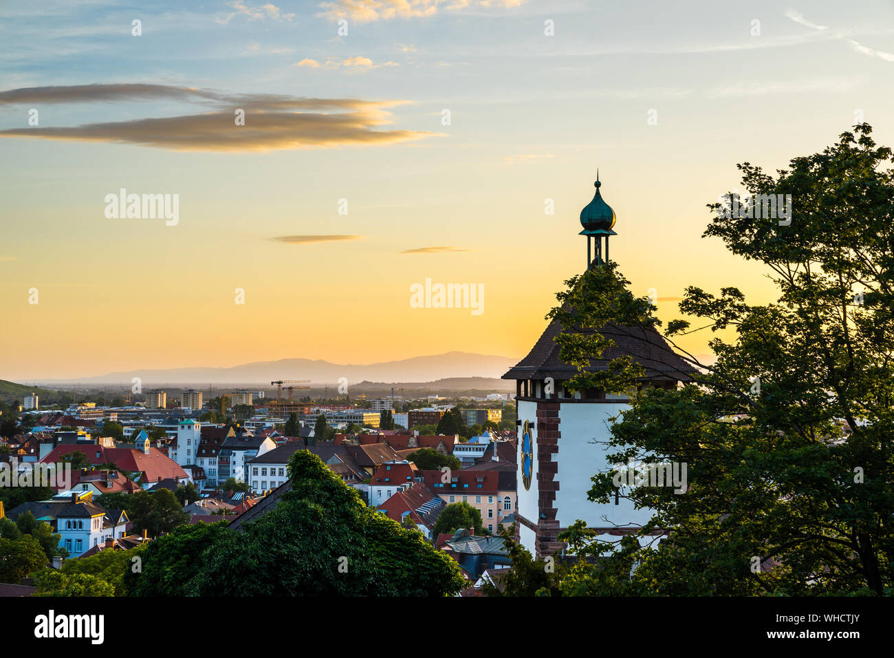 Germania, vista sopra i tetti della città di Freiburg im Breisgau sopra schwabentor, svevo town gate in caldo arancio luce del tramonto in vacanza estiva tim Foto Stock