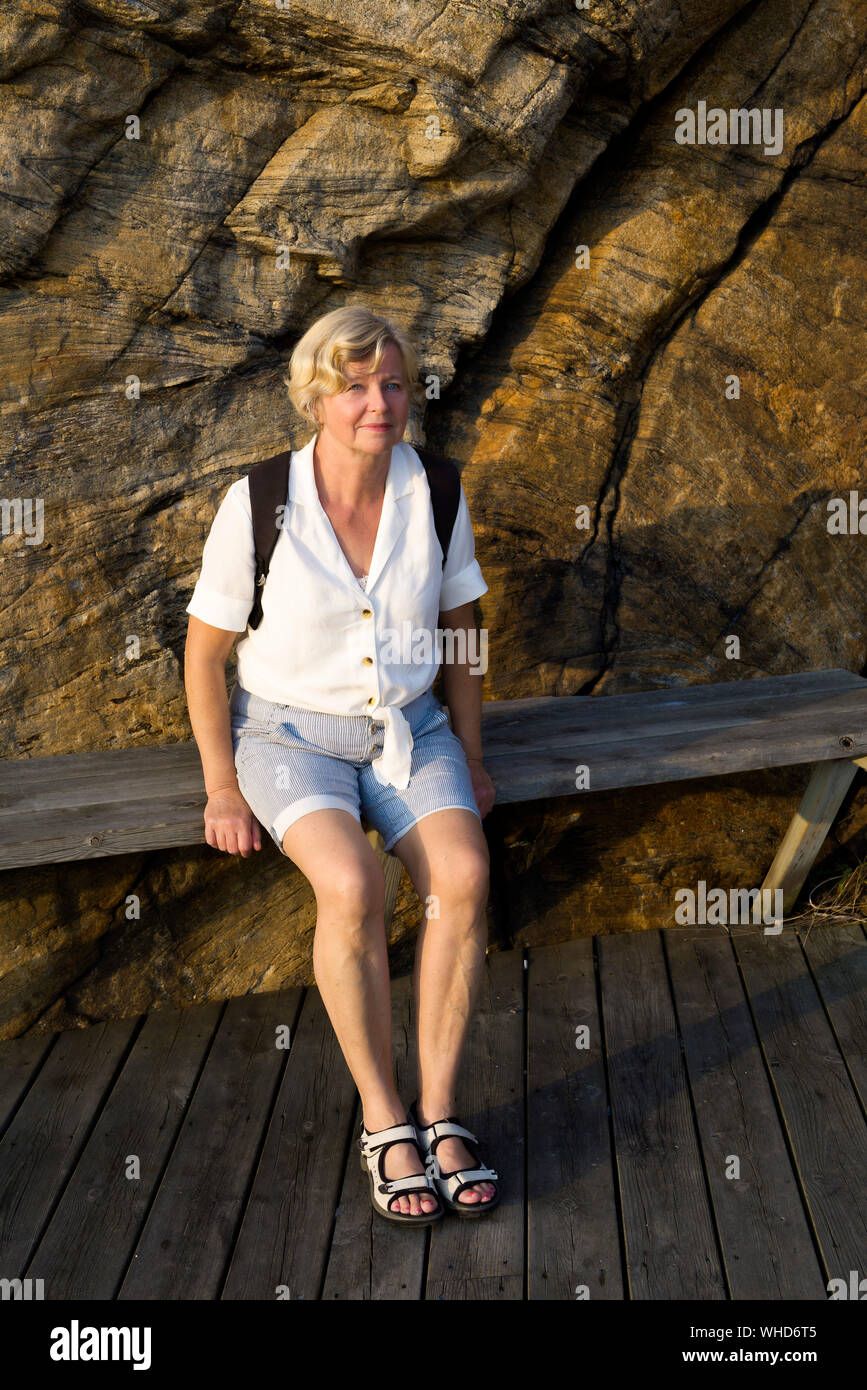 Donna bionda relax su una panchina lungo il porto in Smögen nella soleggiata una sera d'autunno Foto Stock