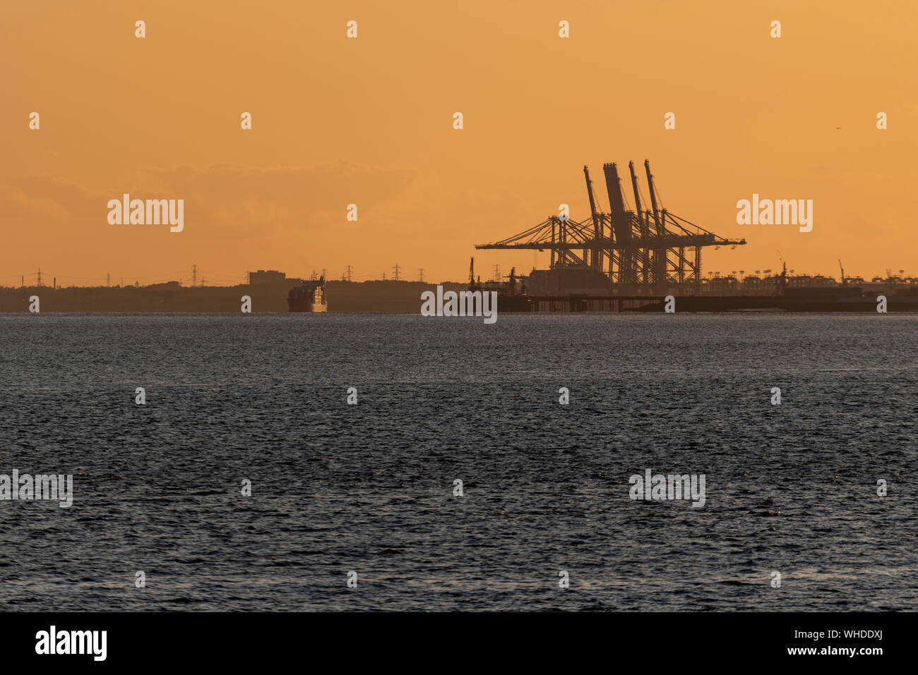 Tramonto dietro Two Tree Island e Canvey Island da Leigh on Sea, Essex con gru portuali DP World London Gateway. Nave portacontainer Foto Stock