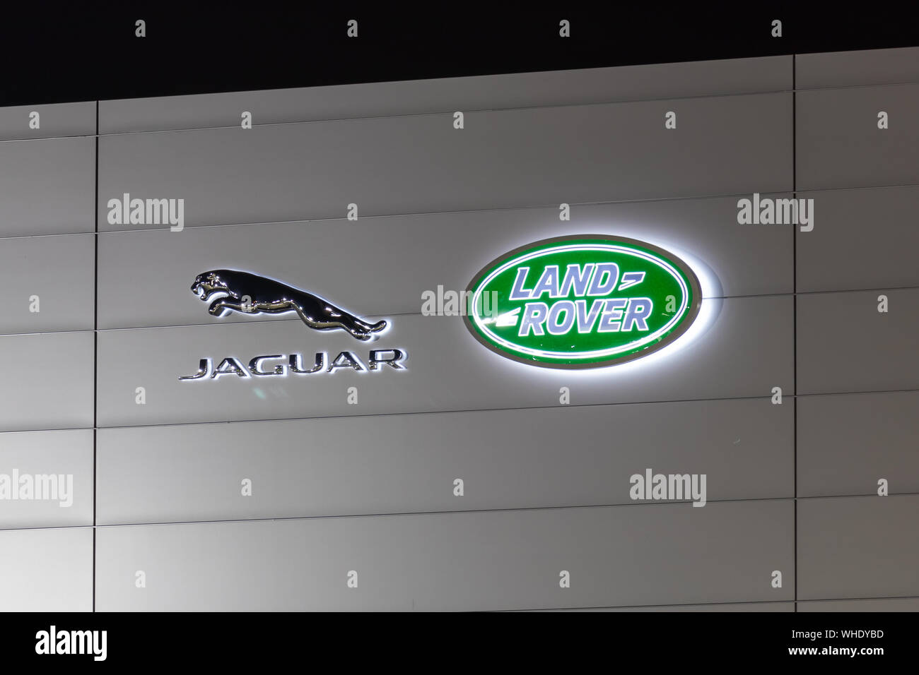 I logo Jaguar e Land Rover sono illuminati di notte sul lato di una concessionaria. Foto Stock