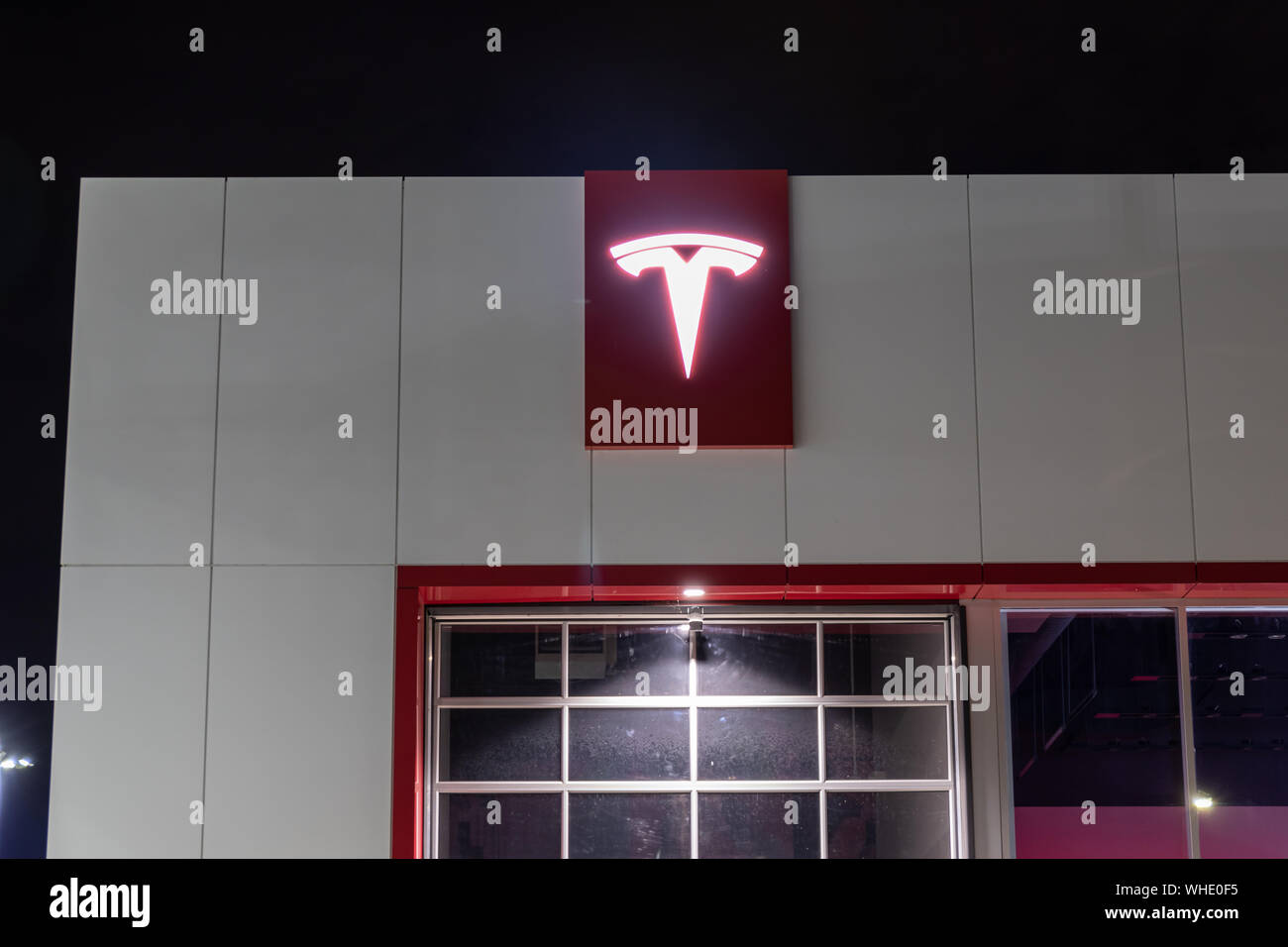 Logo Tesla illuminato di notte in cima a una concessionaria Tesla. Foto Stock