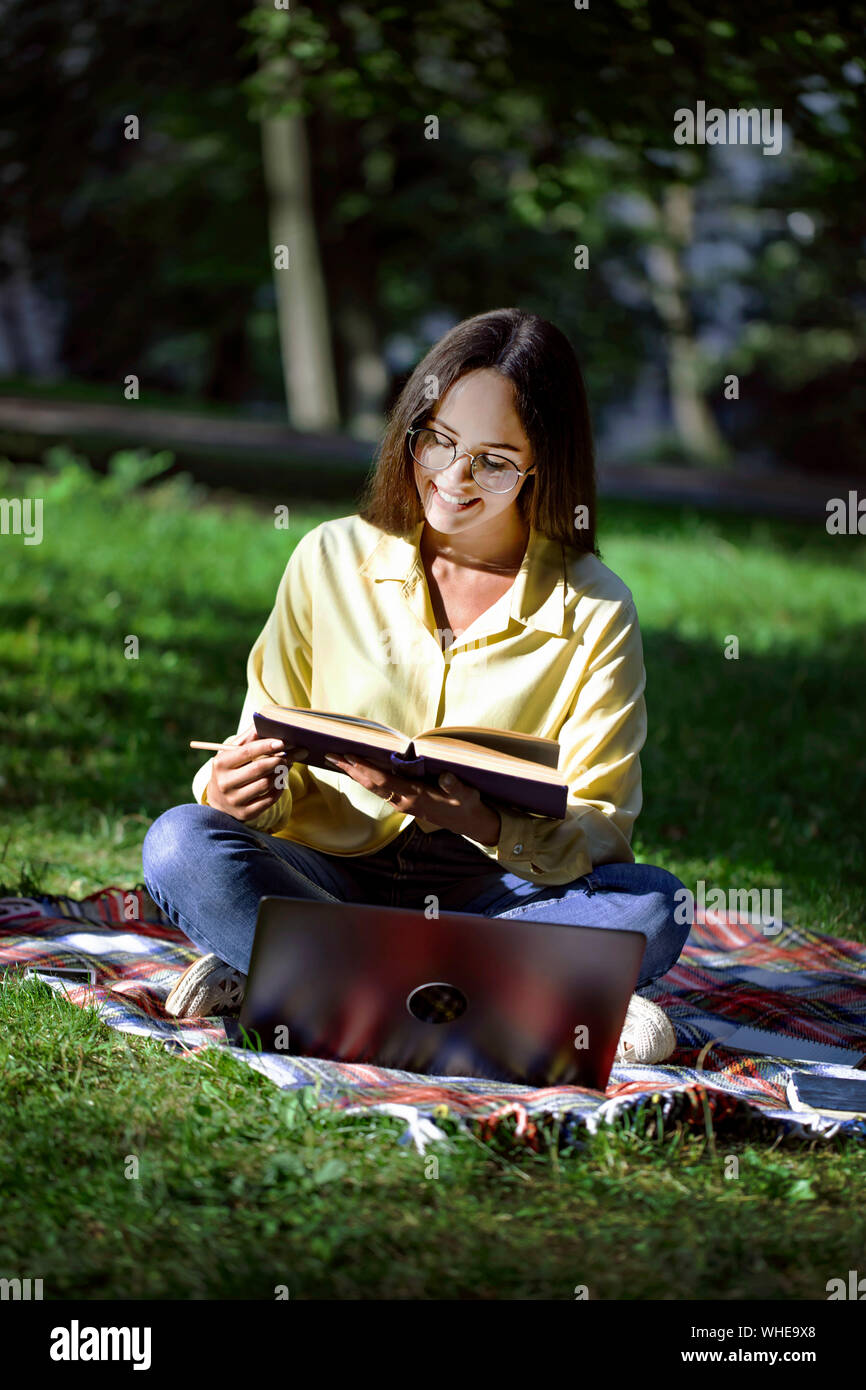 Carina ragazza studente la lettura di un libro seduti su un tappeto nel parco del campus Foto Stock