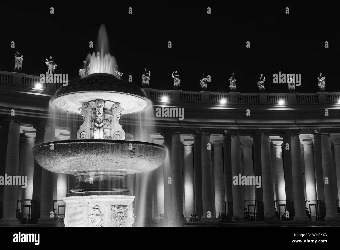 Foto in bianco e nero di fontana di fronte al Colonnato di Piazza San Pietro in Vaticano durante la notte. Foto Stock