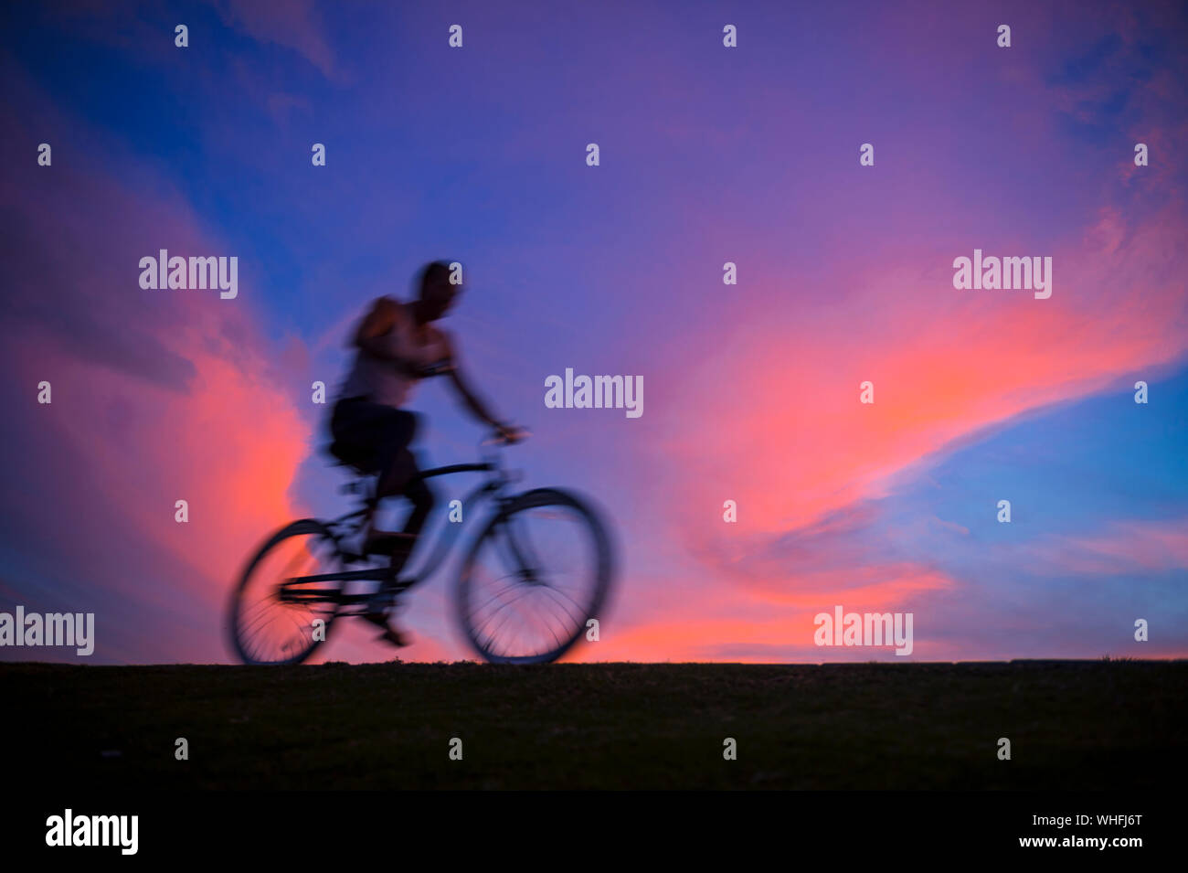Defocalizzazione abstract vista al tramonto di un irriconoscibile silhouette di un uomo in bicicletta in motion blur contro il cielo colorato Foto Stock