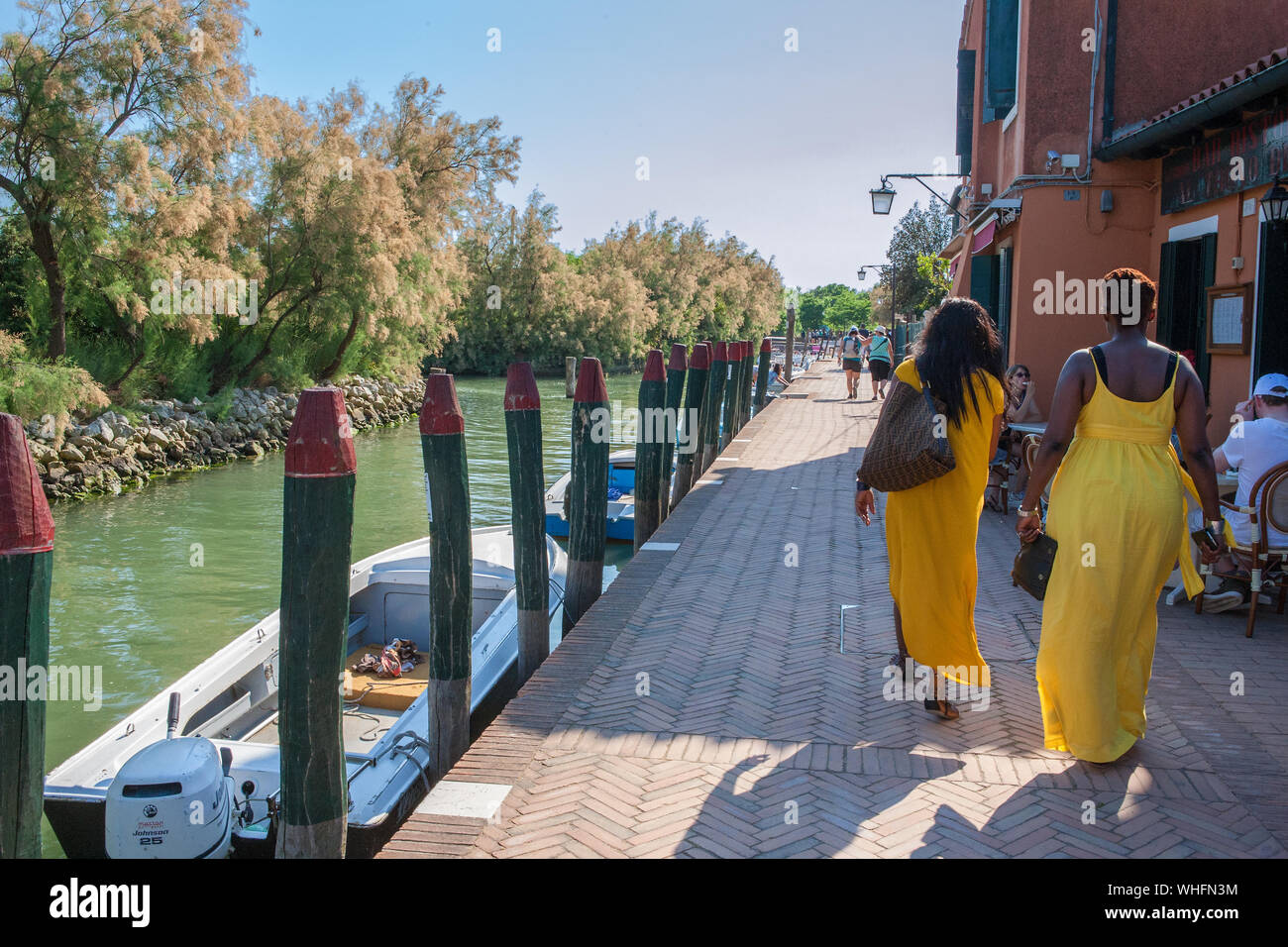Due signore in abiti di colore giallo camminare per la strada della Rosina, Torcello, Venezia, Italia Foto Stock
