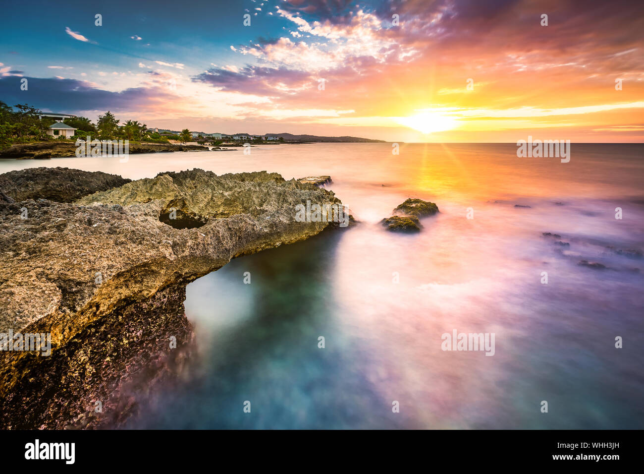 Esposizione a lungo il tramonto tropicale sulla spiaggia rocciosa in Giamaica Foto Stock