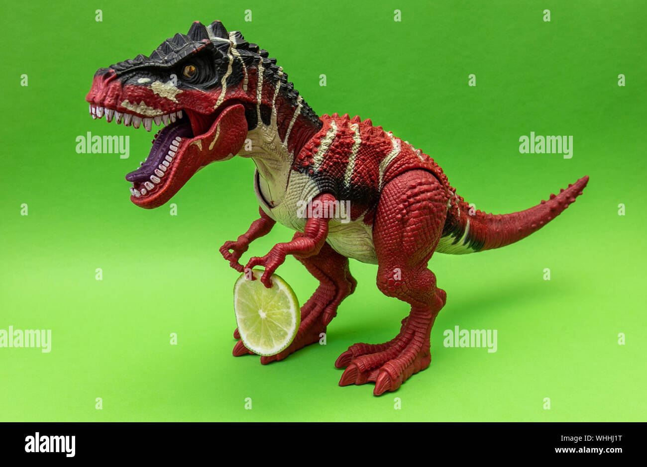 Rosso Tyrannosaur dinosauro con fetta di lime, isolato su sfondo verde, copia spazio per il testo Foto Stock