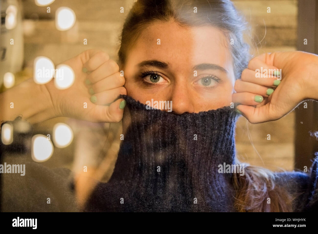 Ritratto di donna che ricopre la faccia con Turtleneck maglione visto attraverso il vetro Foto Stock