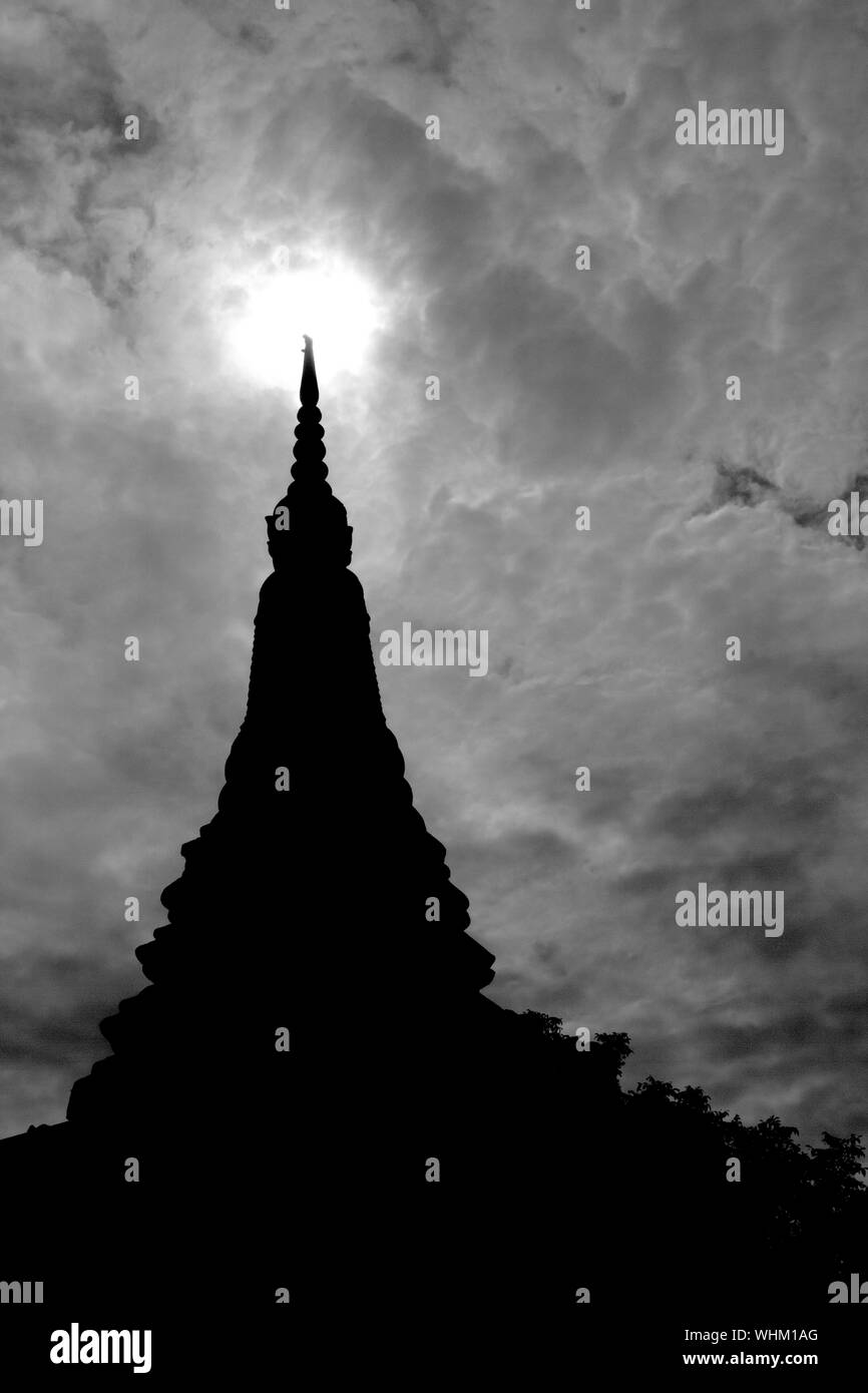 Il piccolo tempio in un villaggio cambogiano. Un cielo nuvoloso con il sole che sorge dove sembra di essere in contatto con la parte superiore del tempio è fatto in bianco e nero Foto Stock
