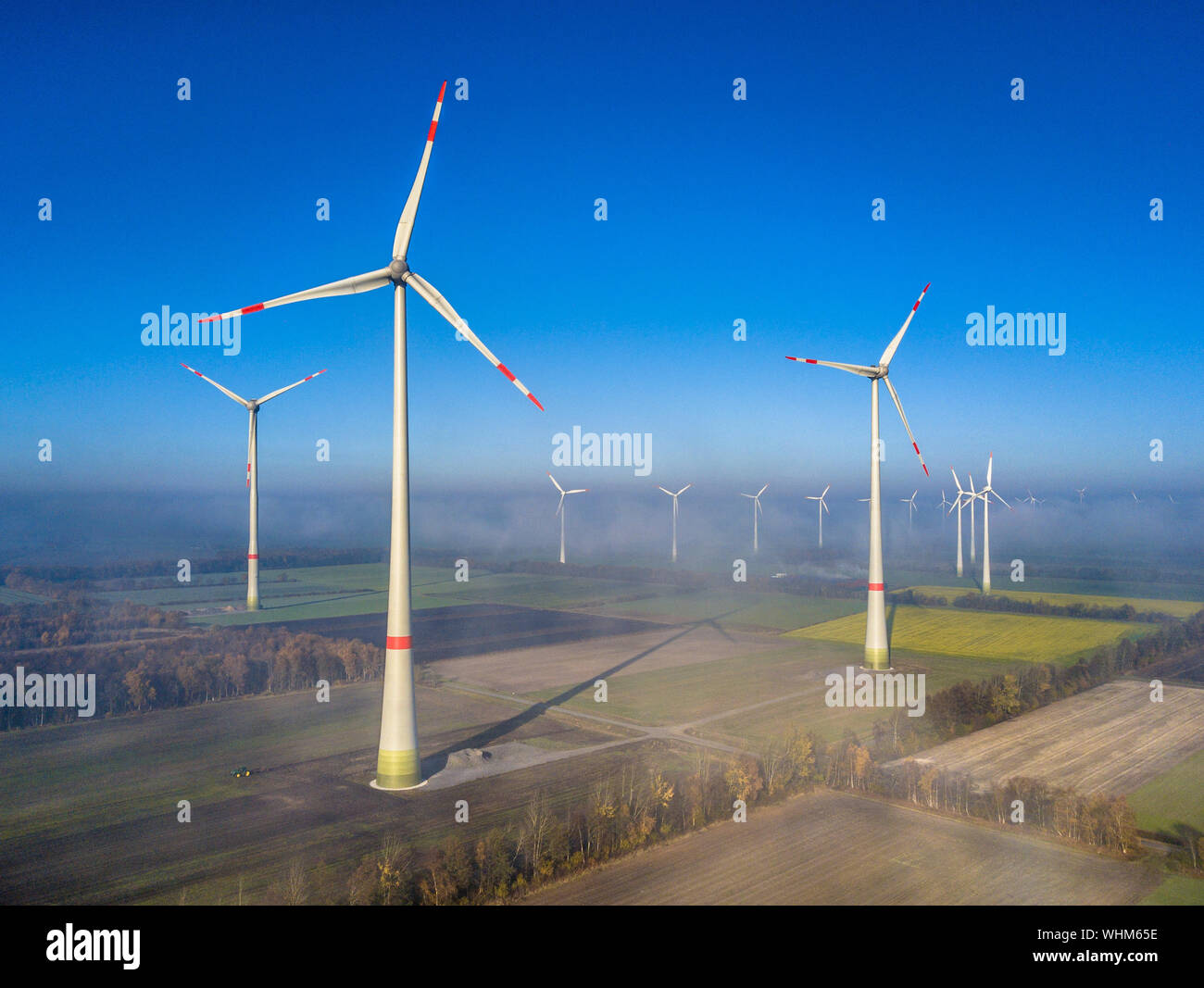 Vista aerea dell'energia eolica turbine di centrali eoliche sopra lo strato di nebbia sulla campagna tedesca al sole del mattino. Germania Foto Stock