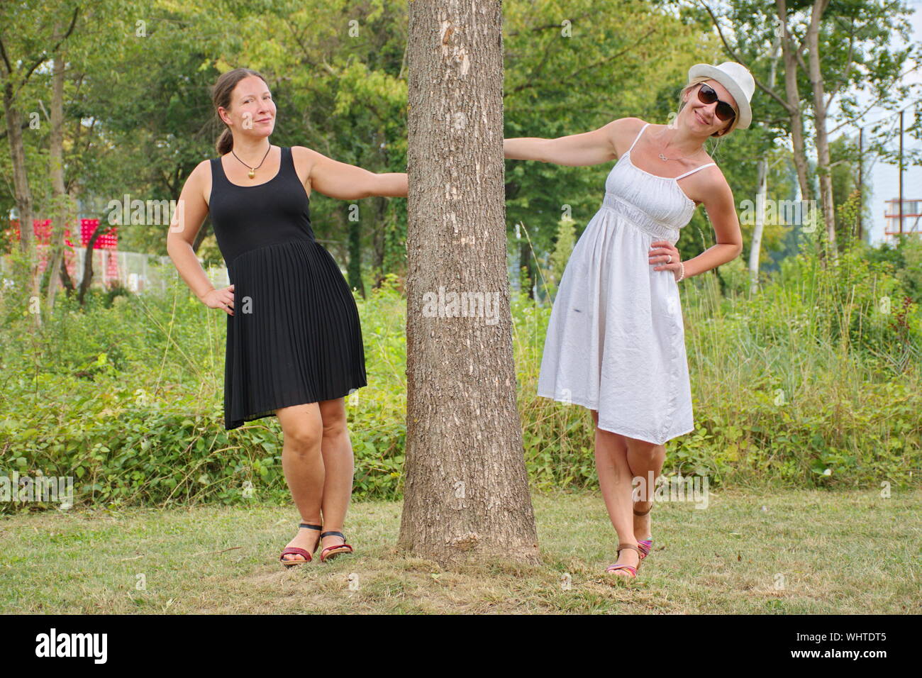 Ritratto di giovane donna con il bianco e nero vestito in posa con la struttura ad albero nel parco Foto Stock