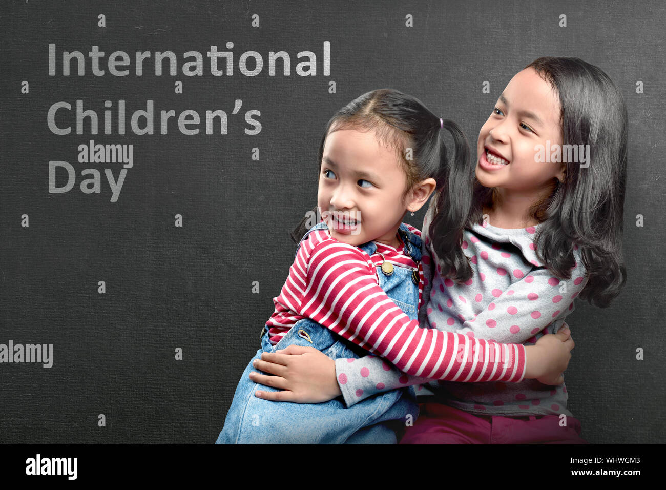 Due Asian cute ragazze abbracciando con muro nero lo sfondo. Internazionale dei bambini al giorno Foto Stock