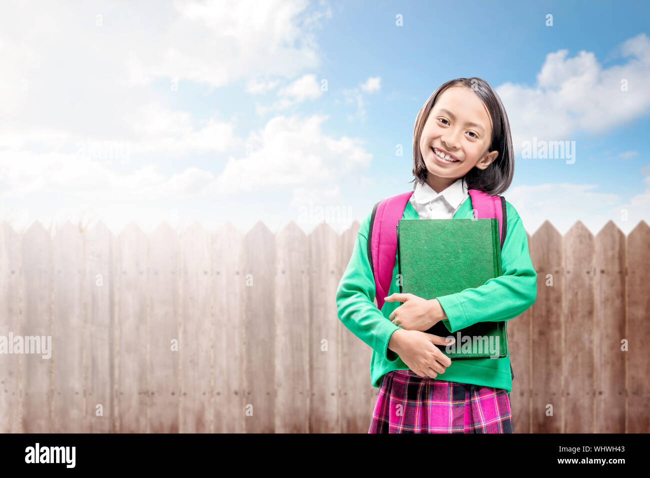 Asian Italian con uno zaino che tiene il libro in piedi con la recinzione di legno sfondo Foto Stock