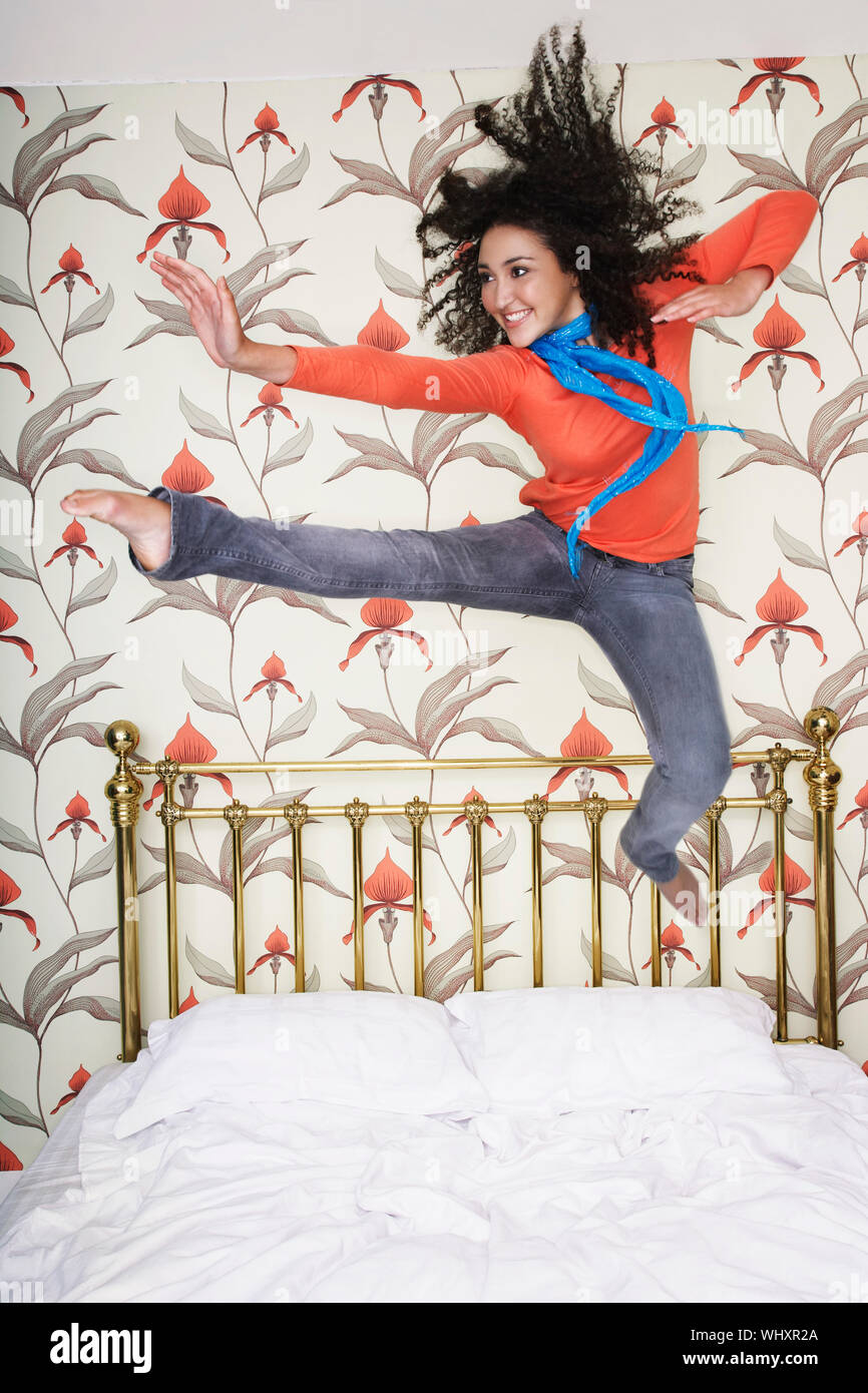 Lunghezza completa di un sorridente ragazza adolescente saltando sul letto Foto Stock