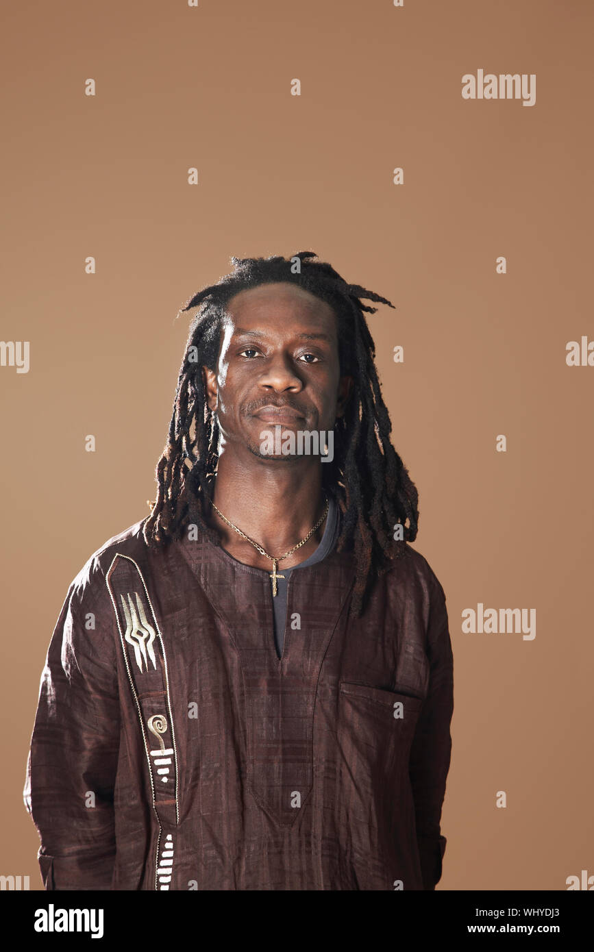 Ritratto di African American uomo con dreadlocks in piedi su sfondo marrone Foto Stock