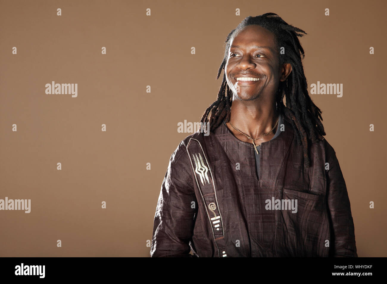 Sorridente African American uomo con dreadlocks che guarda lontano su sfondo marrone Foto Stock