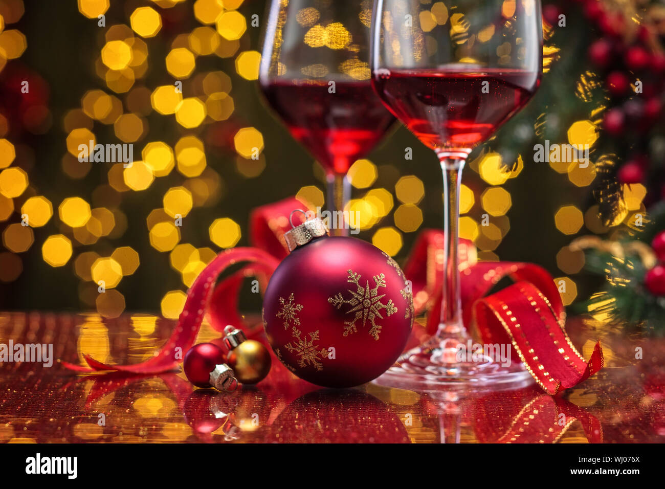 Vino rosso in wineglasses e palla di Natale contro le luci delle vacanze sfondo. Foto Stock