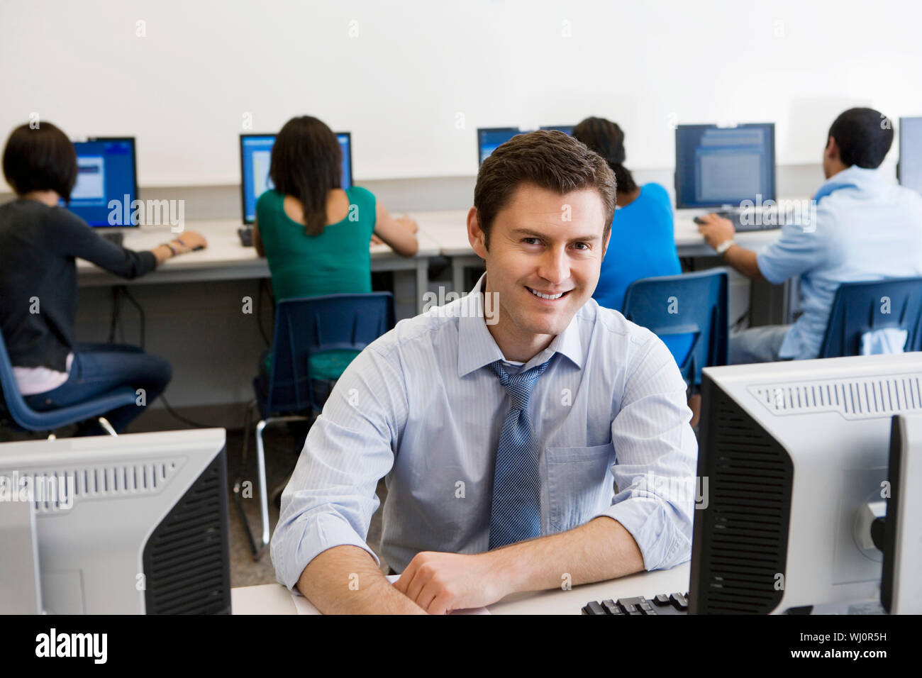 Ritratto di un felice di mezza età professore con gli studenti in laboratorio informatico Foto Stock