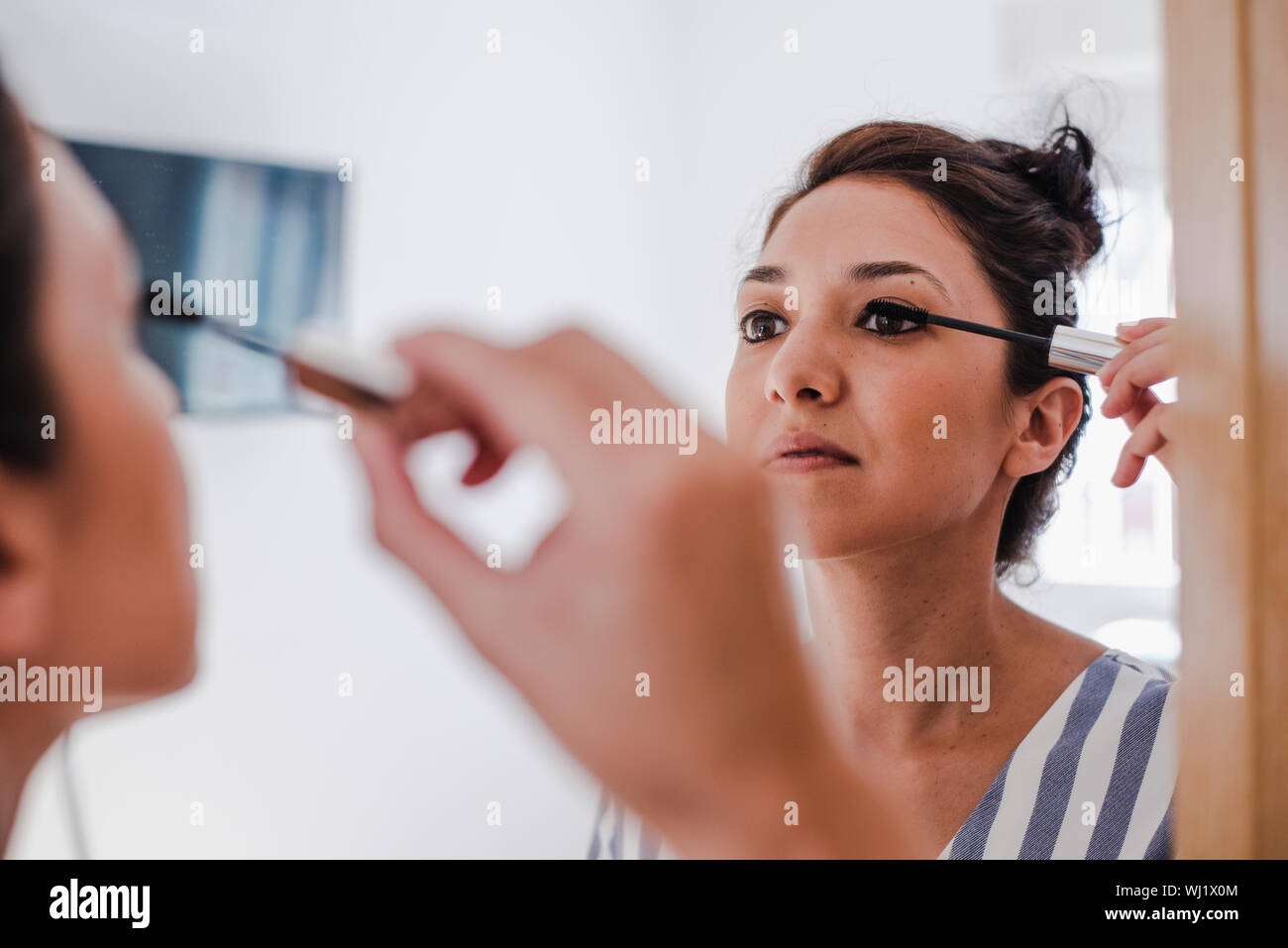 Giovane Latina mettendo su specchio di fronte allo specchio con il suo occhio matita di linea Foto Stock