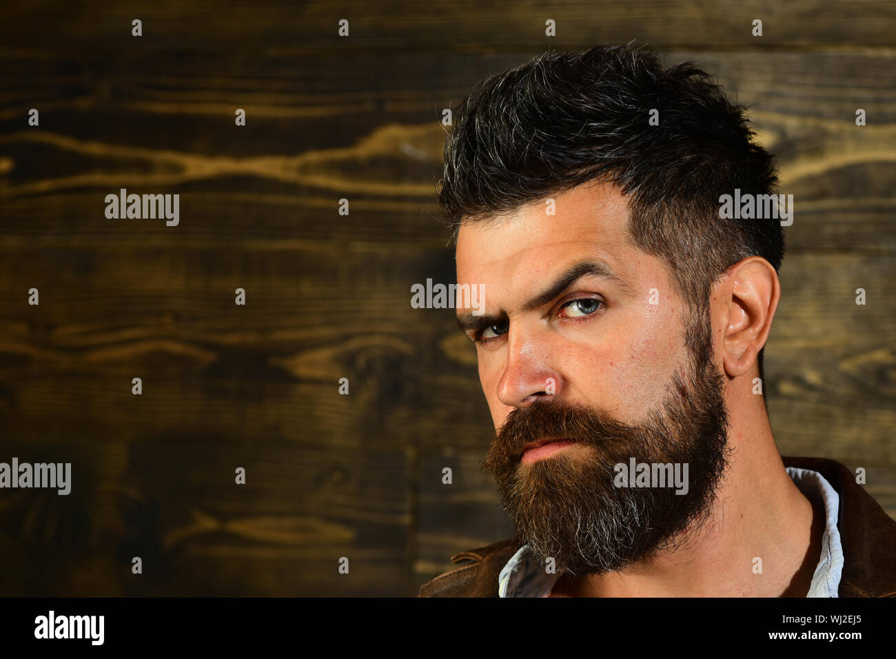 Uomo con barba e baffi su sfondo di legno. Taglio di capelli di uomo barbuto, arcaicità. Moda e bellezza maschile di ingrigimento l'uomo. Barbiere e parrucchiere sal Foto Stock
