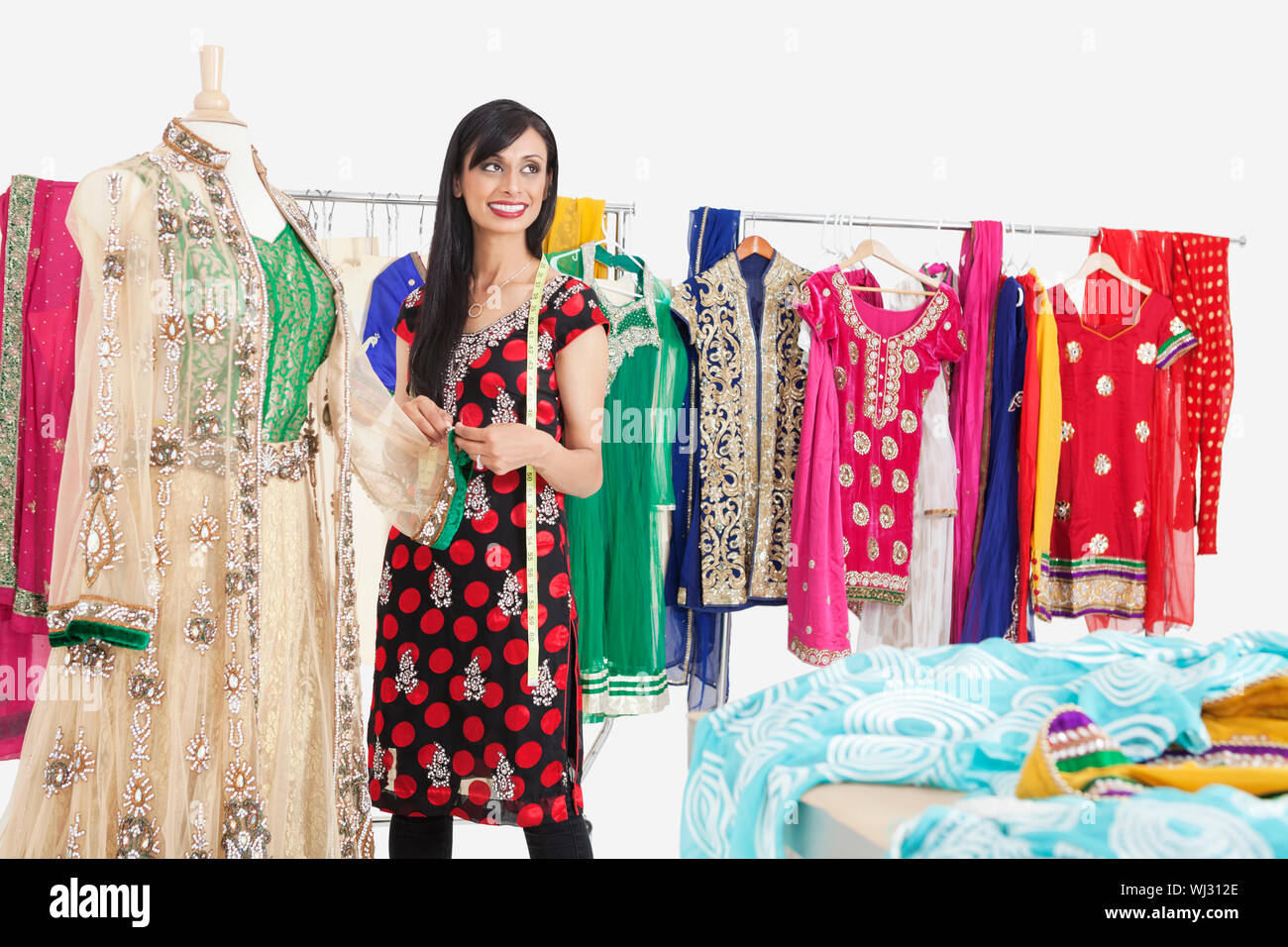 Bella femmina indiano sarta che guarda lontano mentre si lavora sul vestito tradizionale Foto Stock