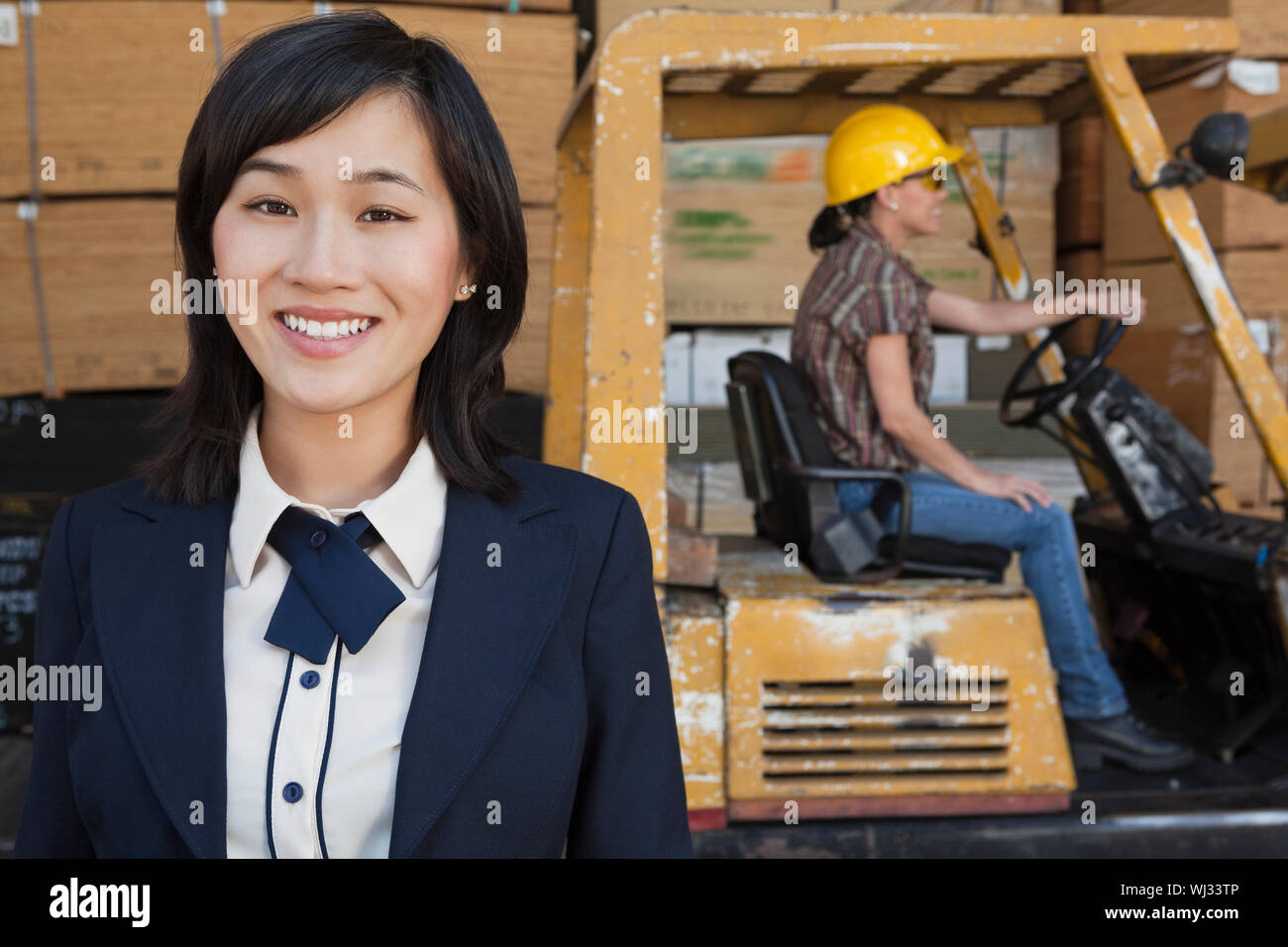 Ritratto di donna sorridente mentre femmina lavoratore industriale la guida carrello elevatore a forche in background Foto Stock