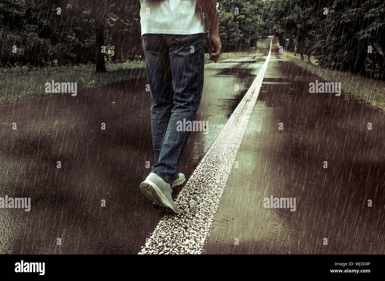 Un uomo n jeans e scarpe da ginnastica a camminare da soli n il park alley  sotto la pioggia Foto stock - Alamy