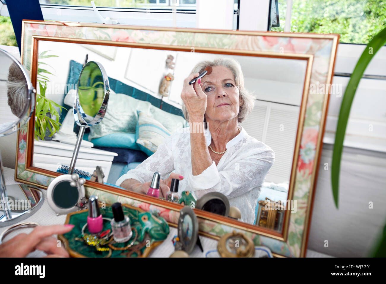 Specchio di riflessione senior donna applicando blusher a casa Foto Stock