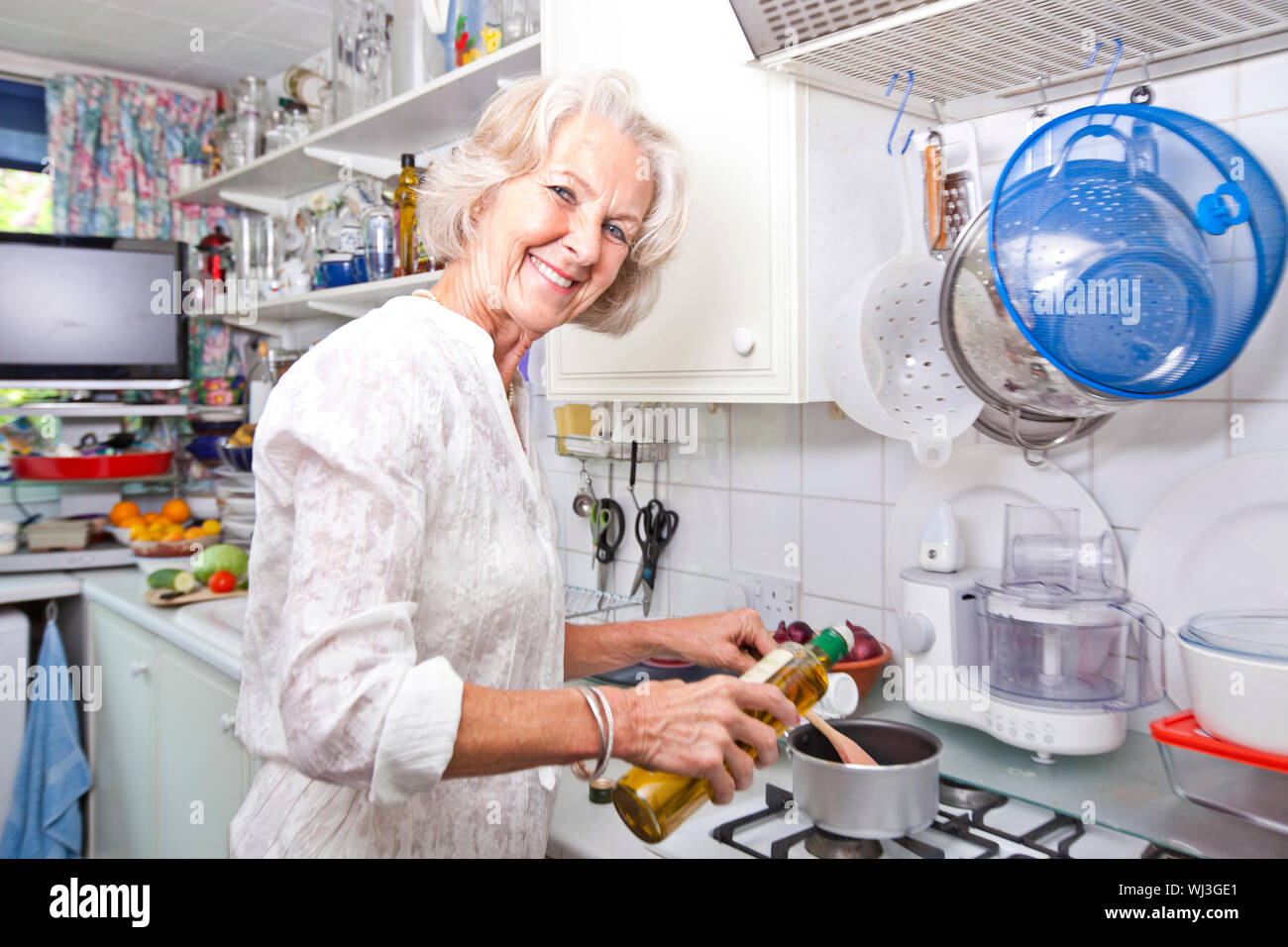 Ritratto di donna senior versando olio d'oliva alla pentola in cucina domestica Foto Stock