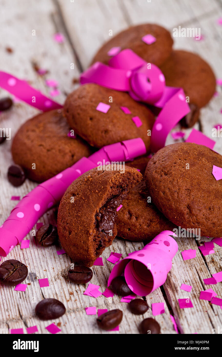 Fresco biscotti al cioccolato, i chicchi di caffè, rosa nastri e confetti sul rustico sfondo di legno Foto Stock