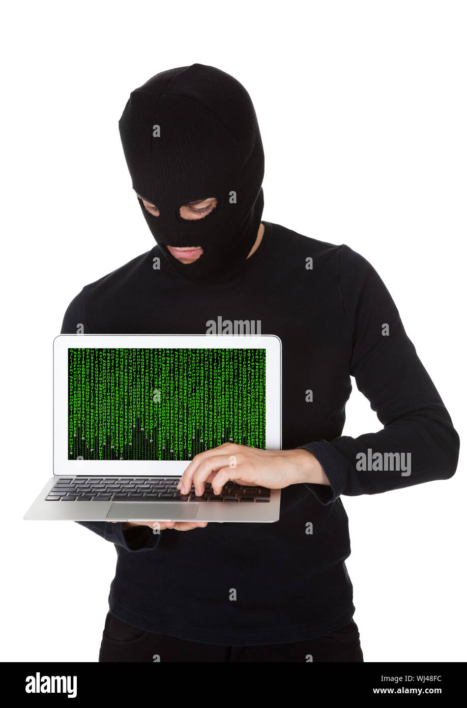 Hacker vestita di nero con una maschera in piedi al furto di dati da un computer portatile con lo schermo rivolto verso la fotocamera in una violazione della sicurezza Foto Stock