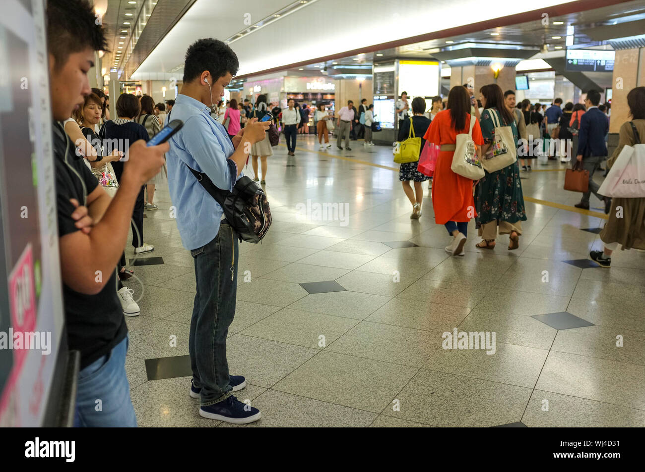 La gente camminare e di controllare i loro telefoni cellulari presso la stazione ferroviaria di Osaka in Giappone. Foto Stock