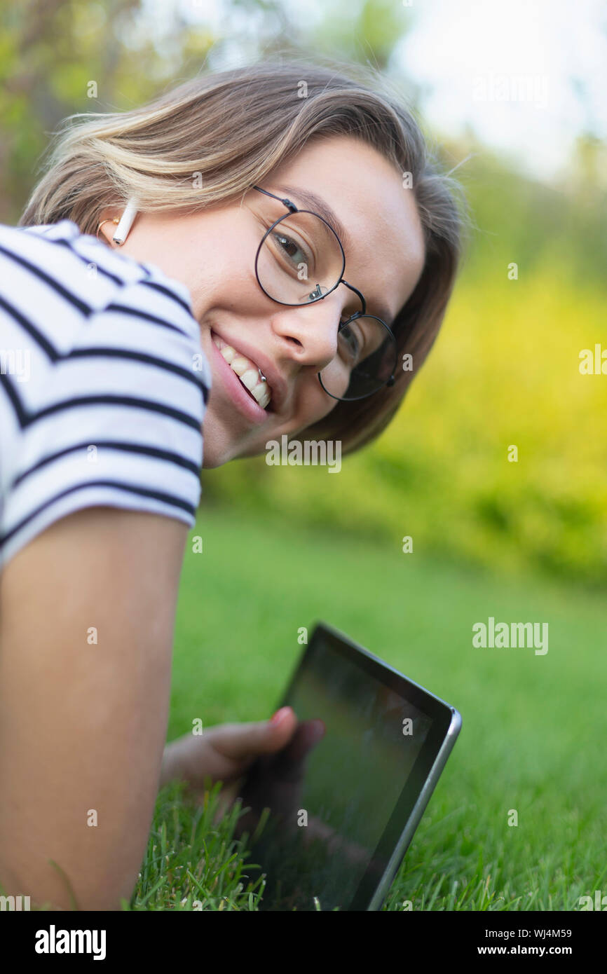 Ritratto sorridente giovane donna con tavoletta digitale e cuffie in erba Foto Stock