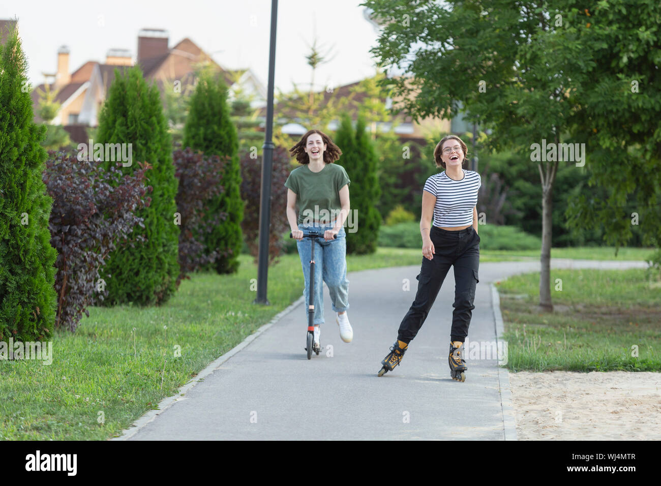 Felici donne amici roller e equitazione scooter push sul marciapiede Foto Stock