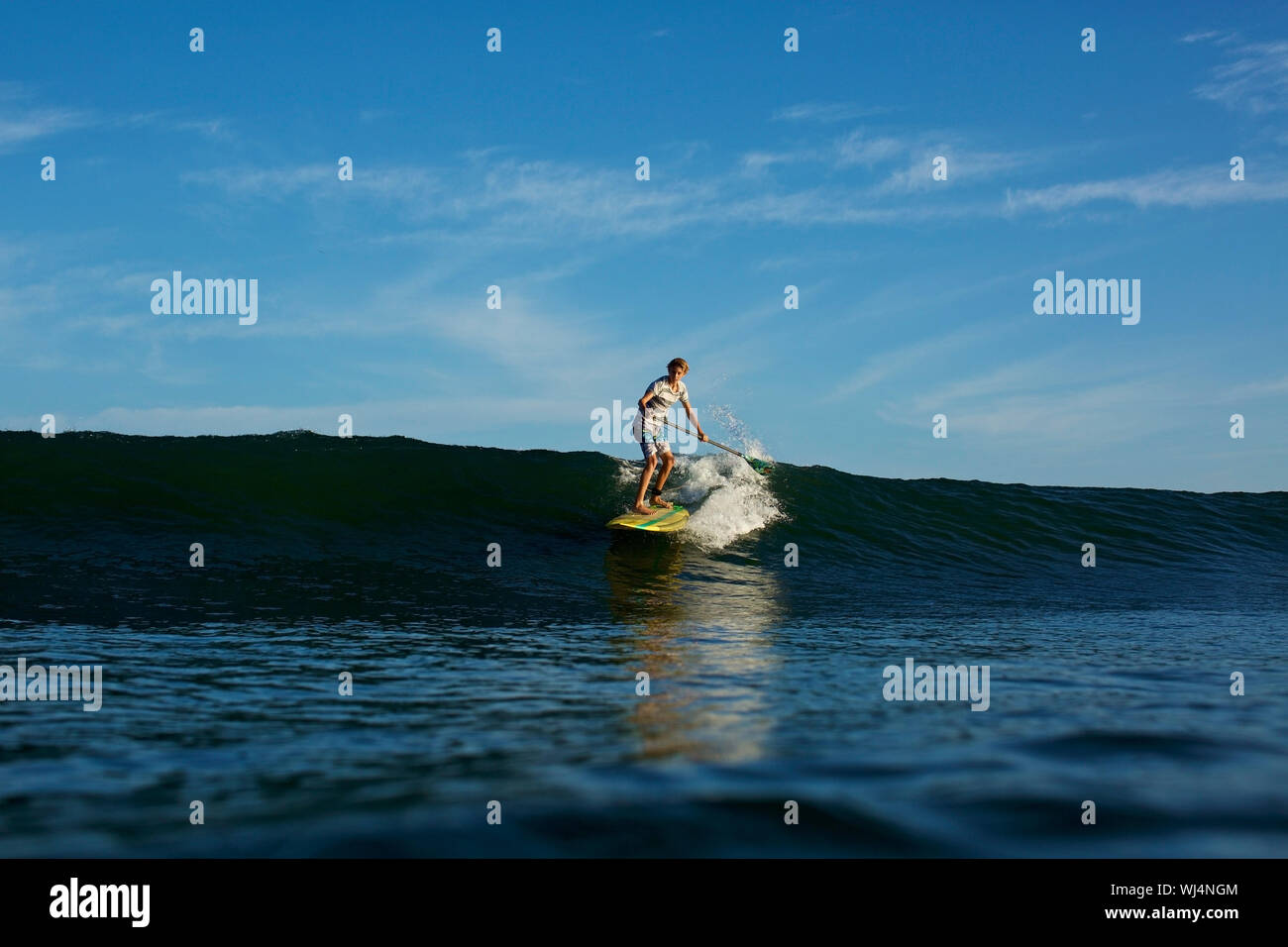 Ragazzo paddle boarder soleggiata di equitazione, blu oceano onda Foto Stock