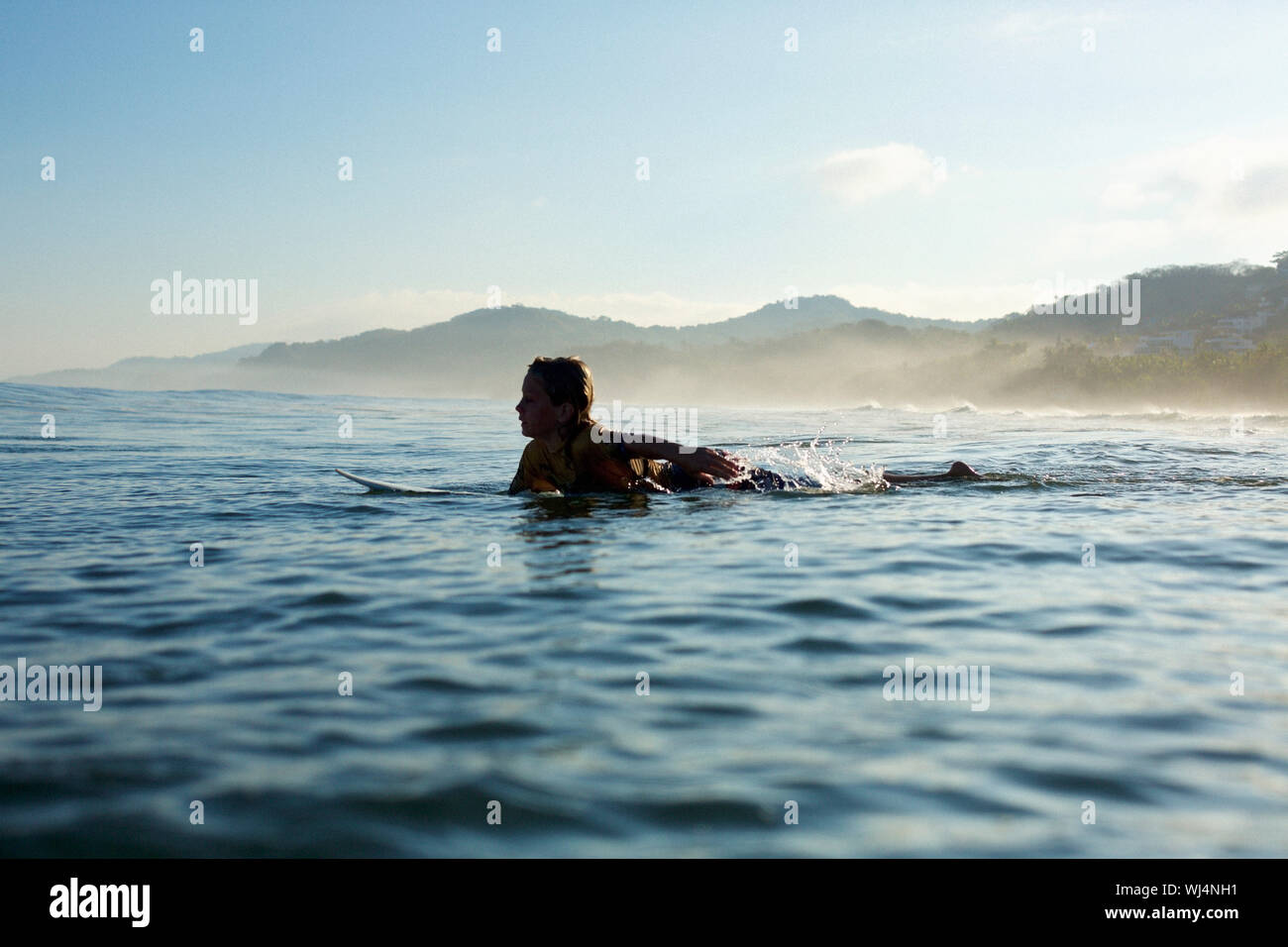 Silhouette boy surfer paddling out sul soleggiato, oceano, Sayulita Nayarit, Messico Foto Stock