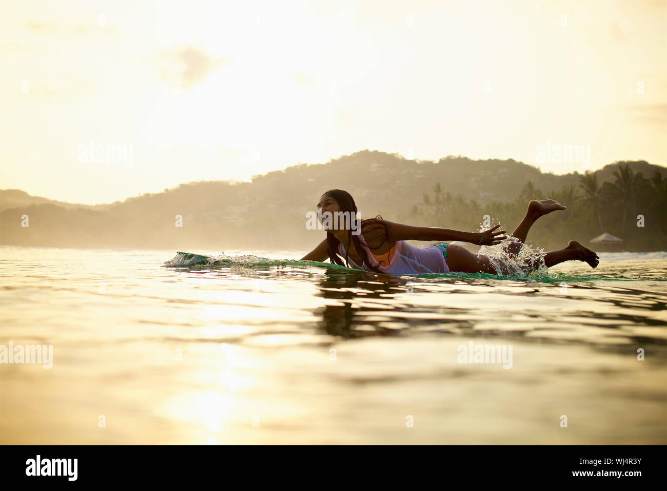 Felice surfista femmina paddling in oceano su tavola da surf, Sayulita, Nayarit, Messico Foto Stock