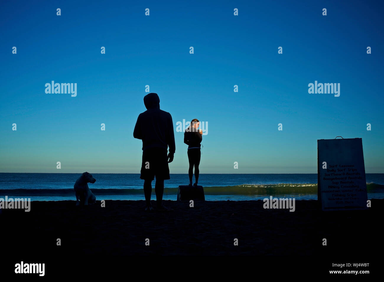 Silhouette giovane coppia con cane sulla spiaggia di sunrise Foto Stock