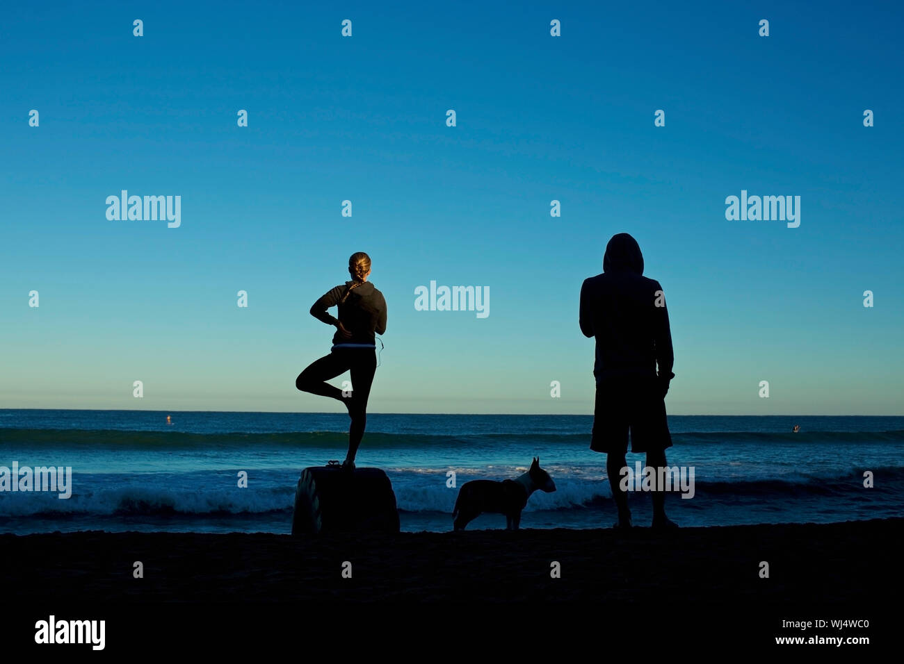 Silhouette coppia giovane con il cane a praticare yoga sulla spiaggia di sunrise Foto Stock