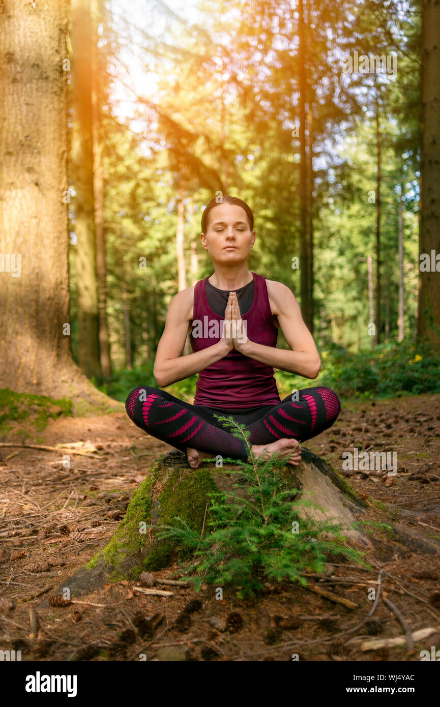 Donna seduta su un ceppo di albero in una foresta meditando, la pratica dello yoga. Foto Stock