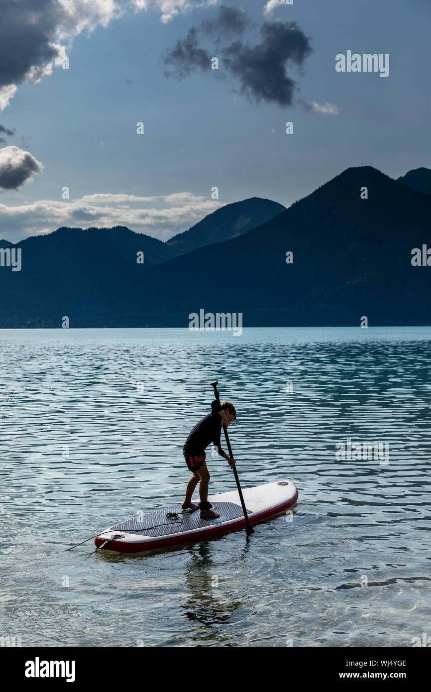 Ragazzo paddleboarding sul soleggiato, idilliaco Lago Walchensee, Baviera, Germania Foto Stock