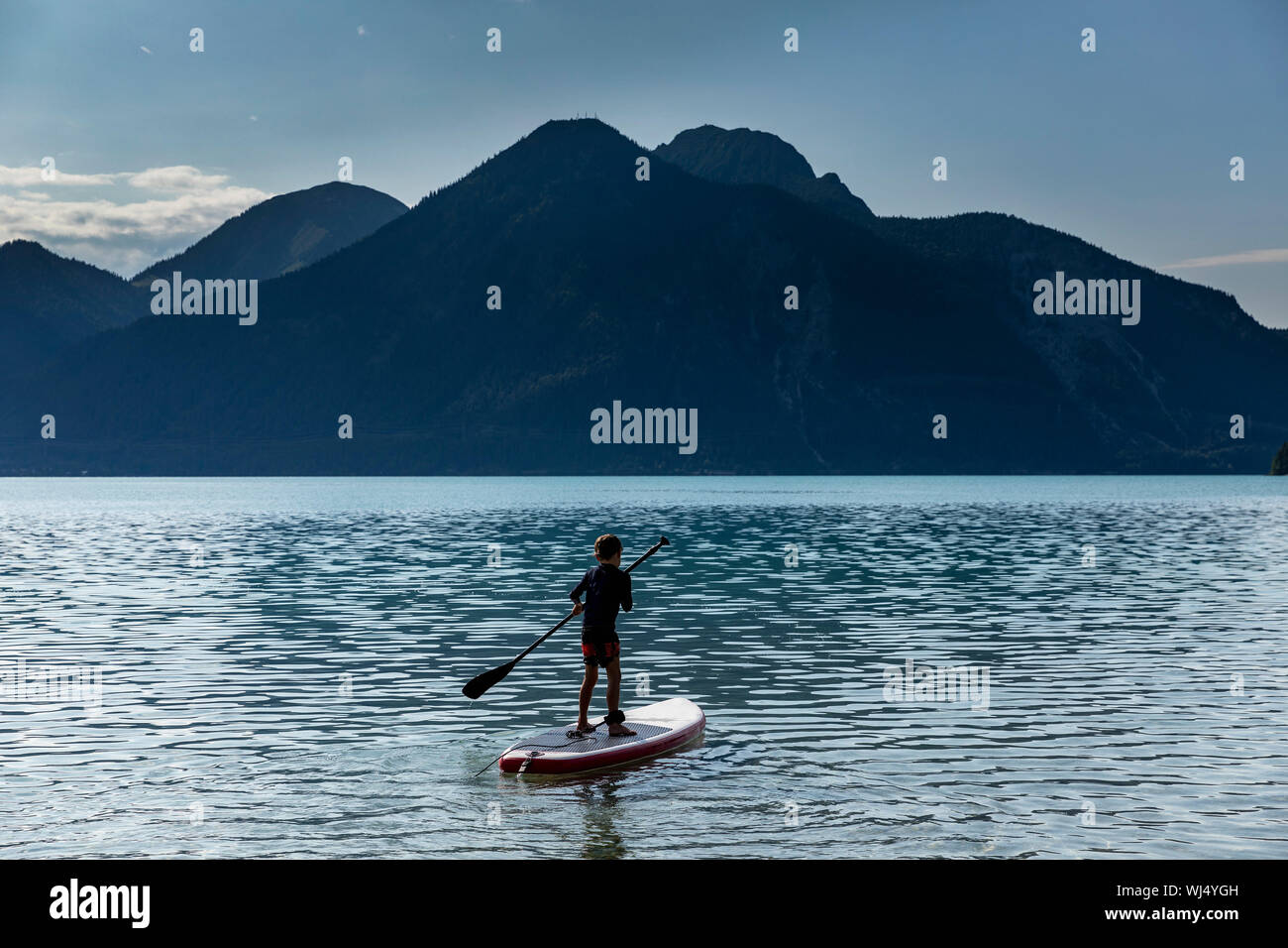 Ragazzo paddleboarding sul soleggiato, idilliaco lago di montagna, Walchensee, Baviera, Germania Foto Stock