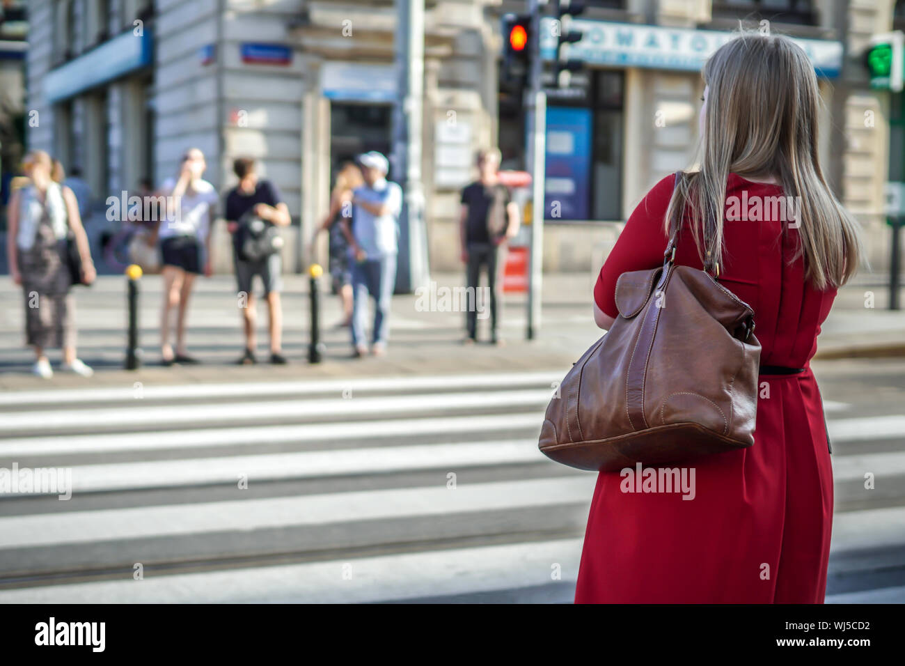 Una donna non identificato in piedi da sola il semaforo, in procinto di attraversare la strada. Foto Stock