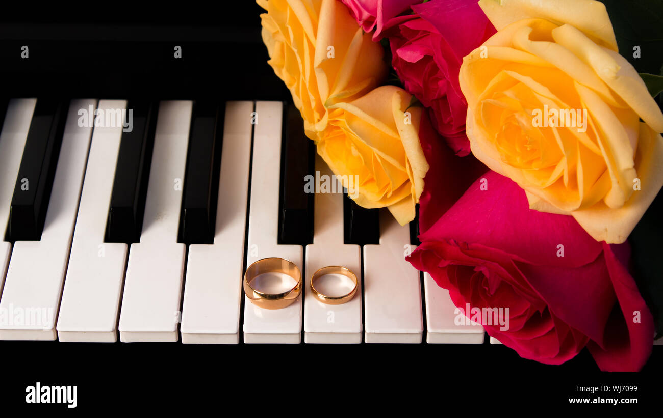 Mazzo di rose giacente sul piano con gli anelli di nozze. Giallo e rose rosse regalo di nozze con le fedi. Preparazione per un matrimonio o di San Valentino d Foto Stock