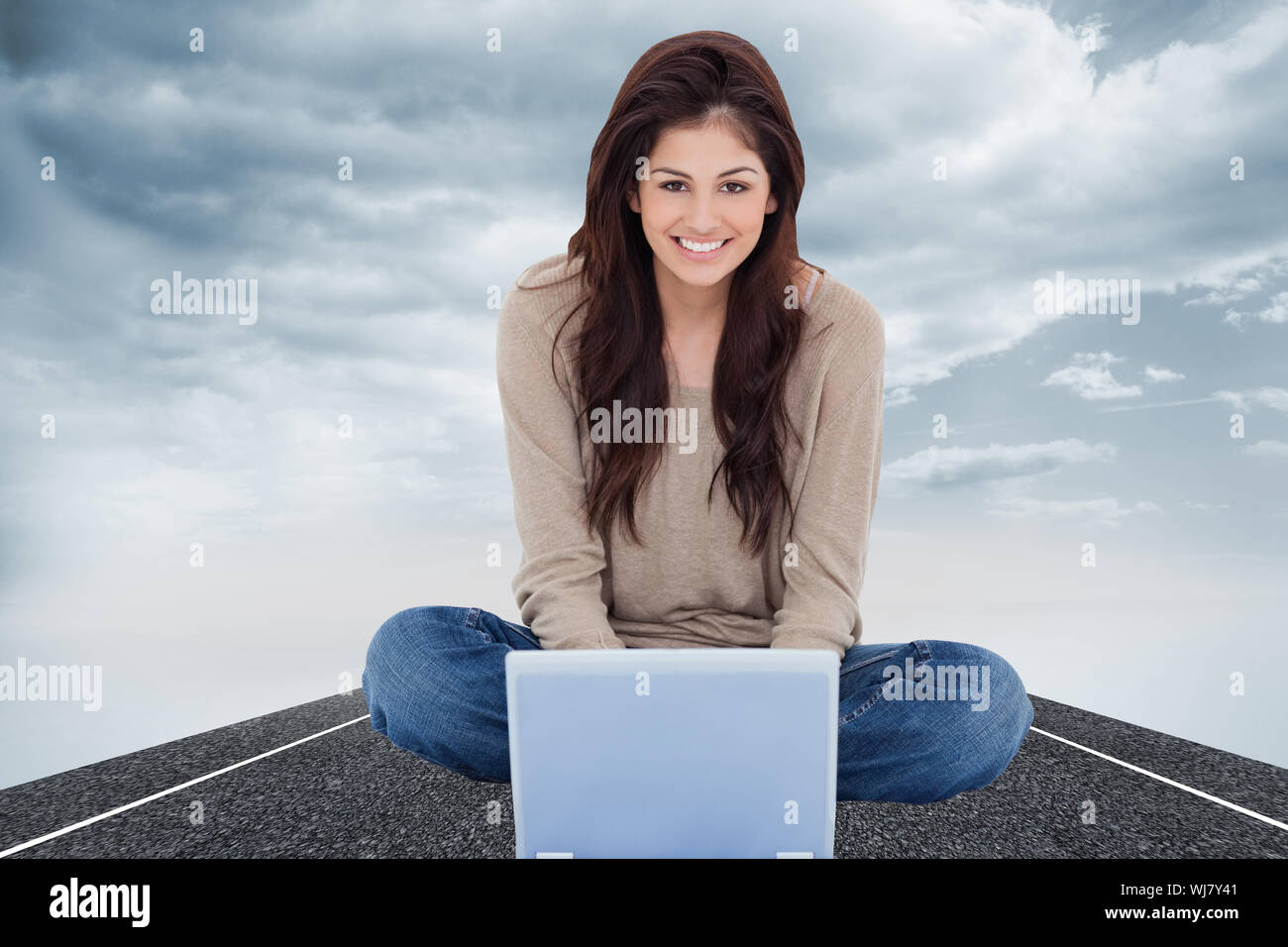 Immagine composita di una donna sorridente come lei si guarda in avanti nella parte anteriore del suo computer portatile con gambe incrociate. Foto Stock