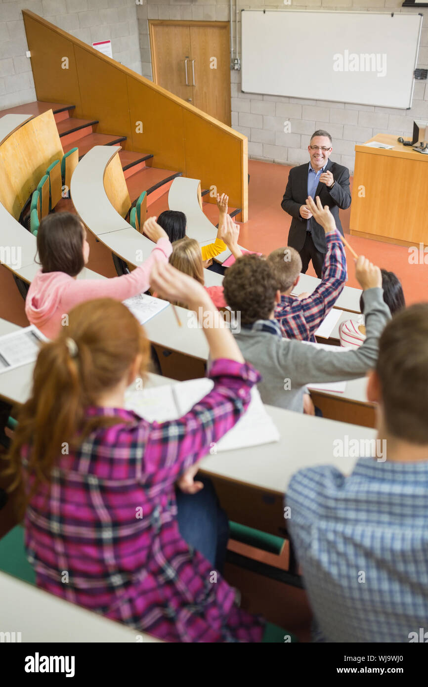 Vista posteriore di studenti alzando le mani con un insegnante nel collegio aula magna Foto Stock